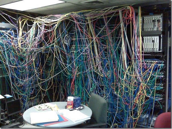 Server room, with a large tangle of wires. In the centre of the room is a table covered with folders, papers, and a large container fo salt.