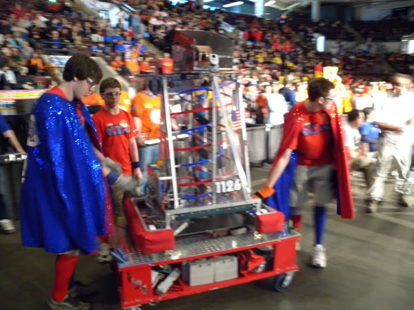 team_in_capes_carrying_robot