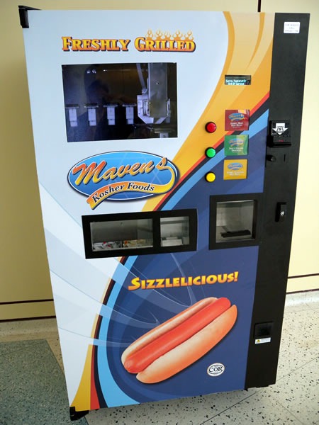 The hot dog vending machine at the Metro Toronto Convention Centre. Its signs say: "Freshly grilled / Maven's Kosher Foods / Sizzlelicious!"