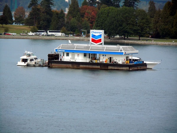 A floating chevron gas station, with a couple of boats moored to it