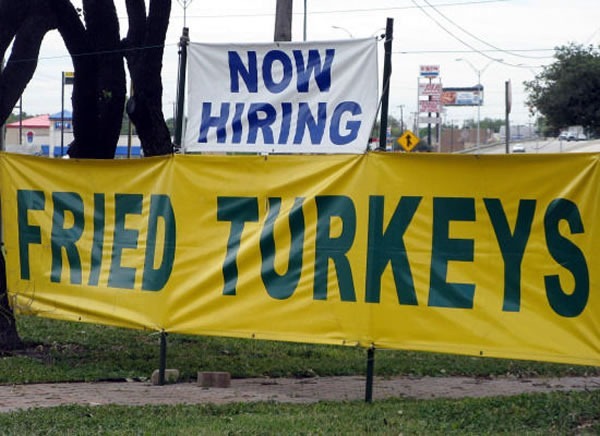 Two signs, one atop the other. Top sign: "Now hiring". Bottom sign: "Fried turkeys"