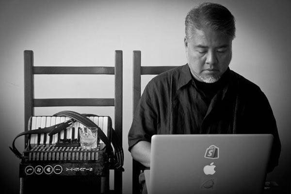 Joey deVilla works on his Macbook Pro, with his accordion and a glass of whiskey by his side.
