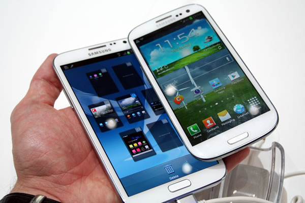 Hand holding both a Samsung Galaxy Note 3 and a Galaxy S4 phone.
