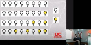 Photo: A slide showing 4 rows of 8 lightbulbs displaying different binary values. Inset in the lower right corner: UC Baseline instructor Tremere lecturing.